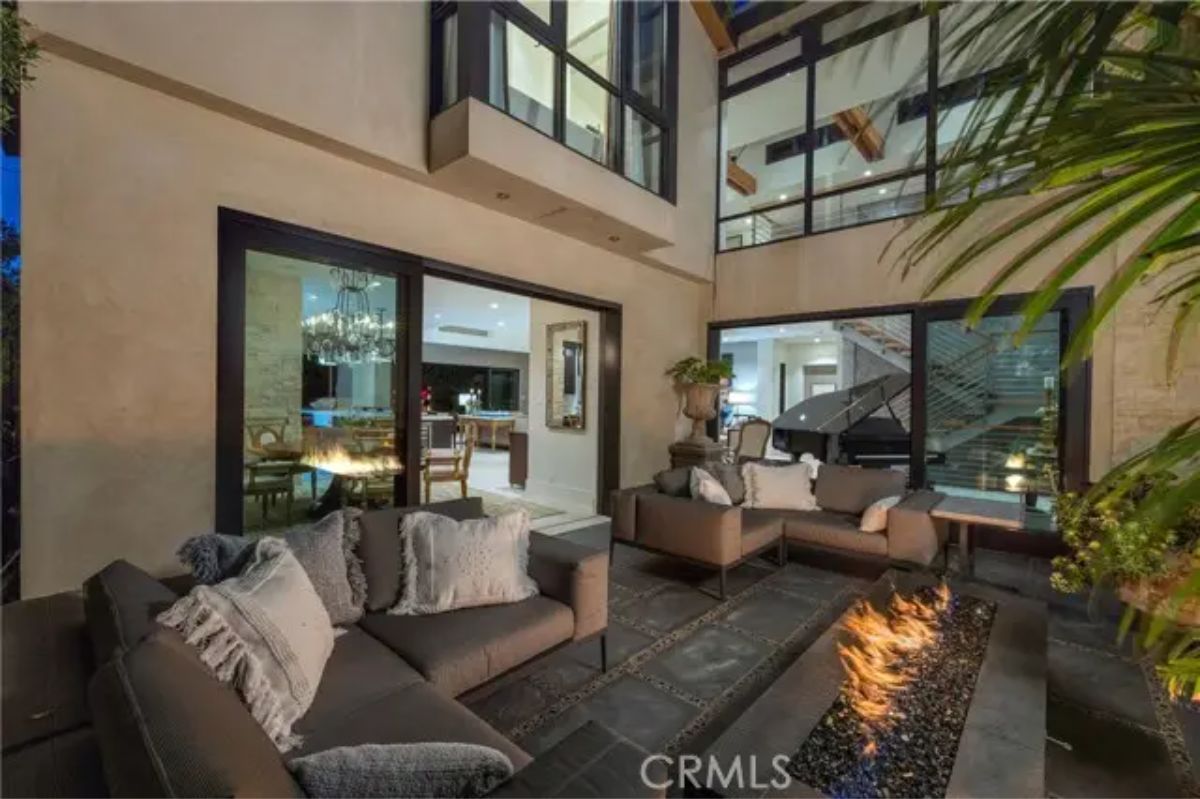 Enclosed outdoor courtyard with cushioned seating, linear fire pit, and nighttime ambiance. 
