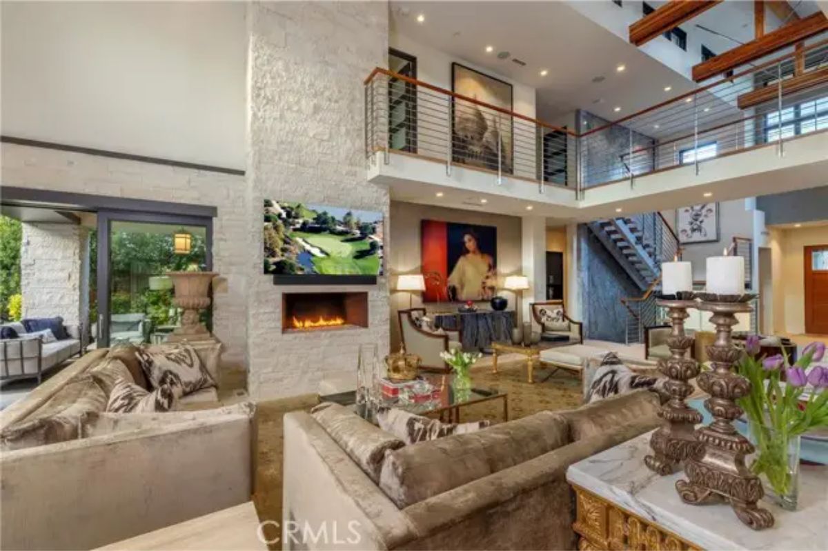 Living room featuring stone fireplace, mounted TV, and balcony overlook. 