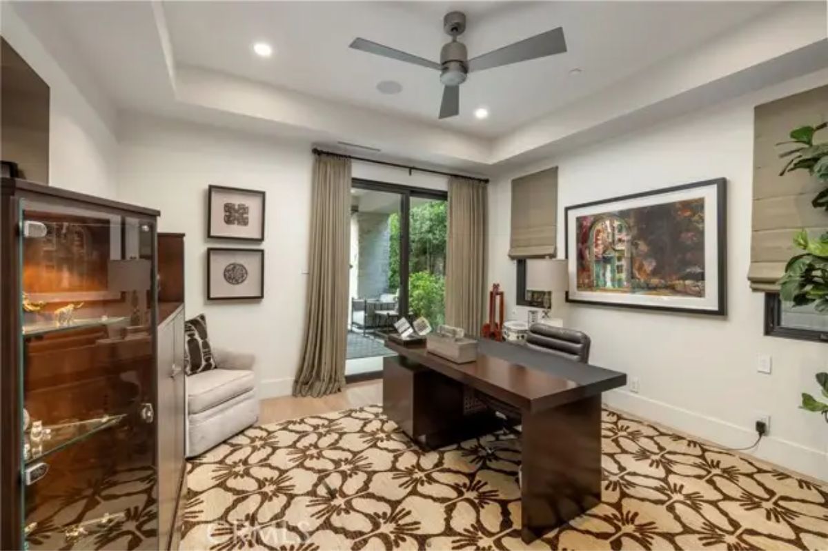Office with tray ceiling, modern desk, patterned rug, and access to patio. 