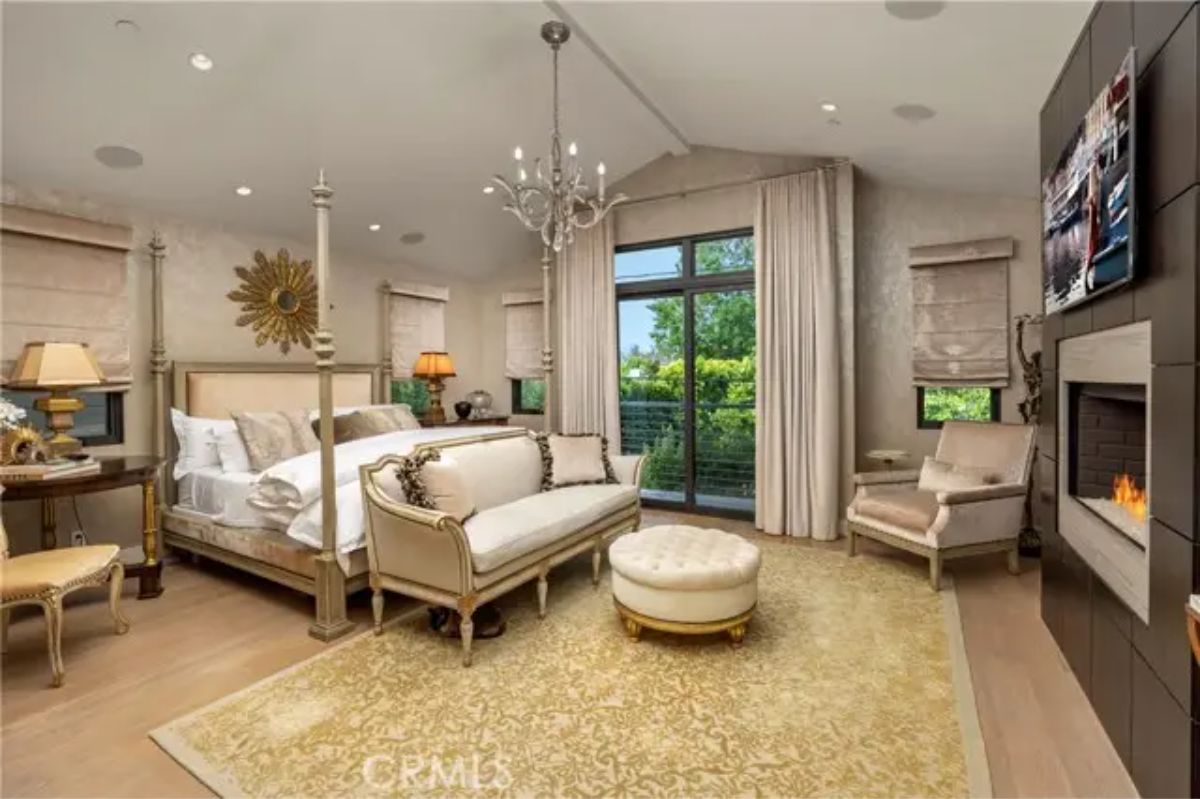 Primary bedroom with four-poster bed, fireplace, chandelier, and private balcony access. 