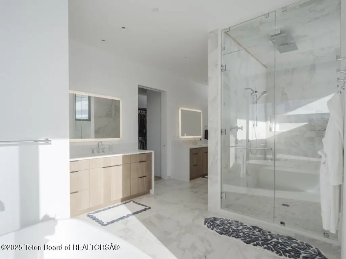 Bathroom with double vanities, marble floors, and large glass-enclosed shower. 