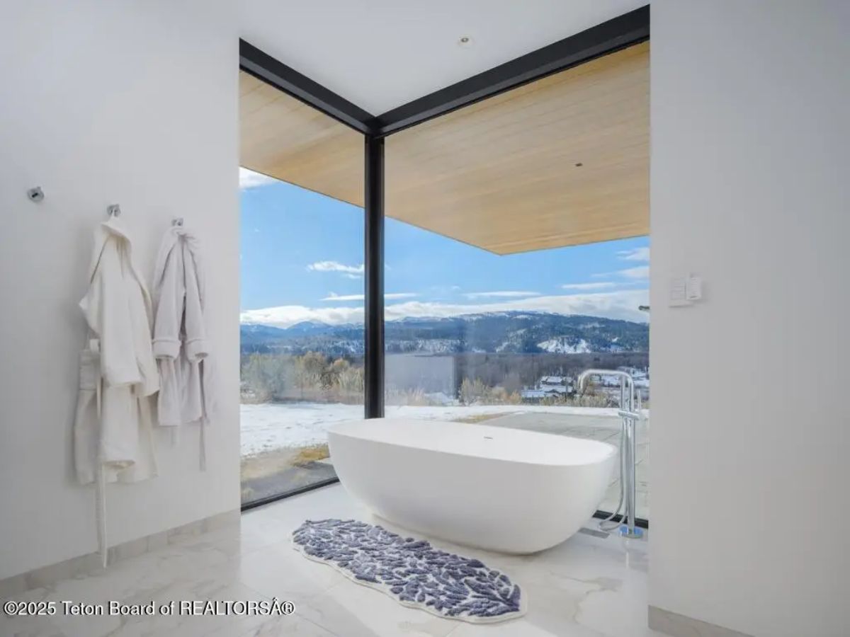Freestanding tub placed in front of corner glass windows offering a serene alpine view. 