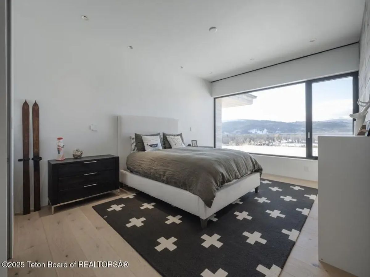 Bedroom with minimalist decor, black-and-white rug, and large window overlooking winter landscape. 