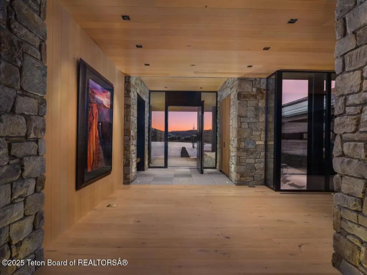 Entry hallway with wood flooring, stone walls, and glass doors framing a mountain sunset view. 