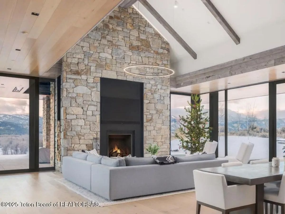 Living room with stone fireplace, large sectional sofa, and sweeping views of snowy mountains. 