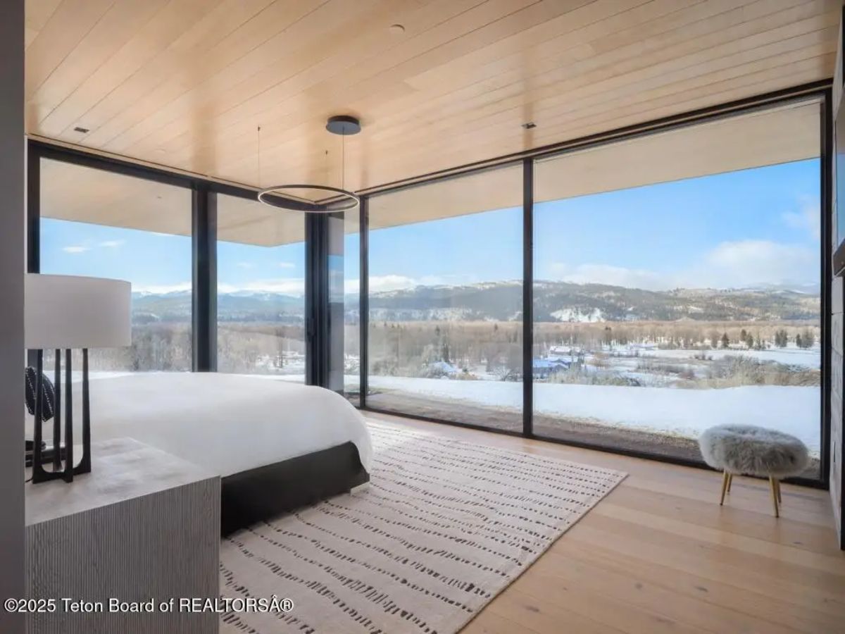 Corner bedroom with wood ceiling and full-height windows showcasing unobstructed mountain views. 