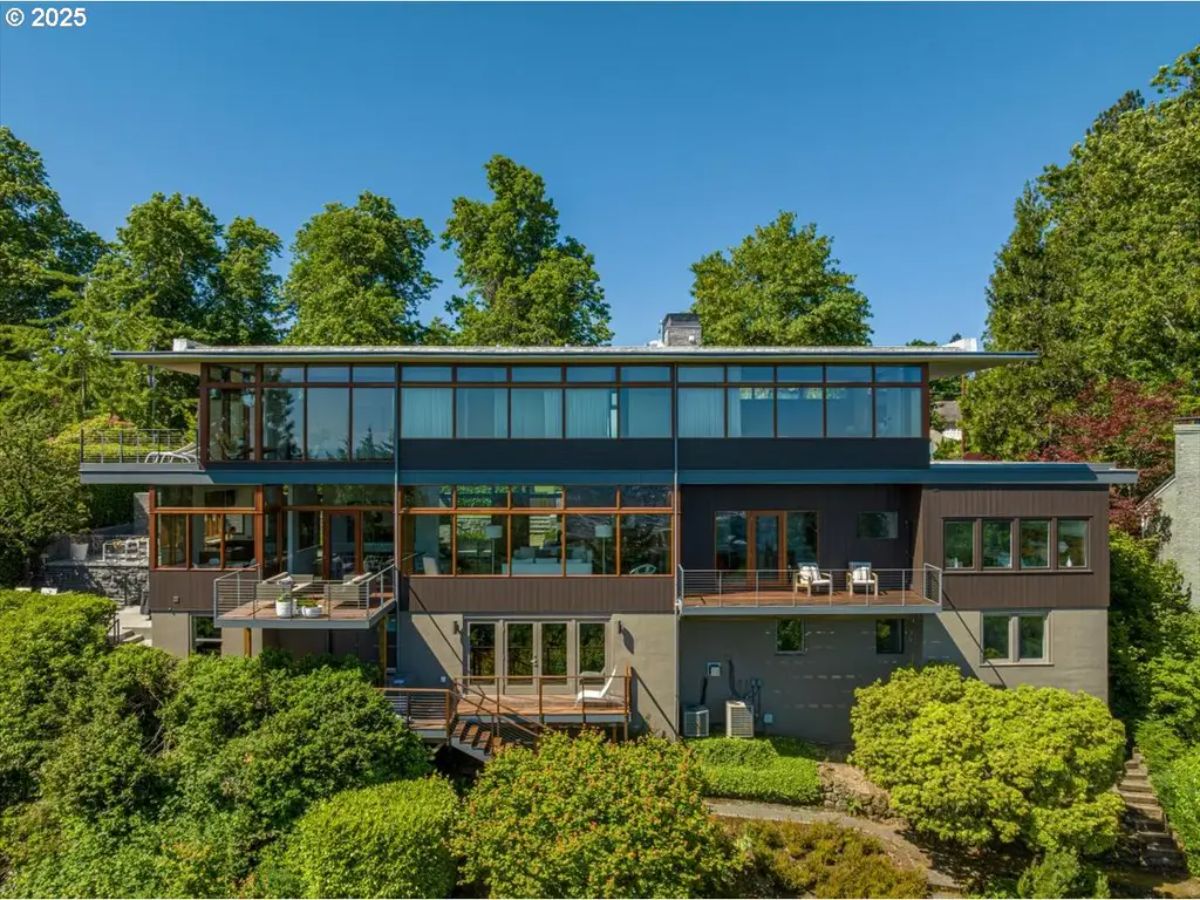 Rear exterior of modern hillside home with expansive windows and multiple balconies. 