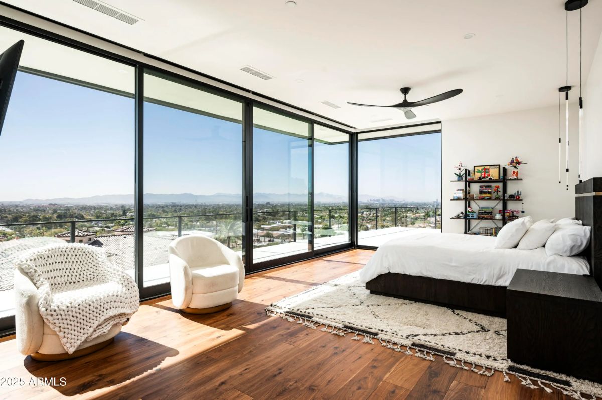 Primary bedroom with floor-to-ceiling corner windows, mountain views, and warm wood flooring. 