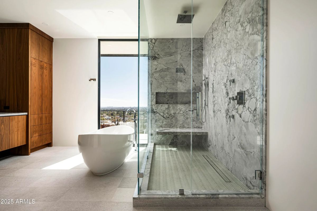 Spa-style bathroom with marble shower, freestanding tub, and floor-to-ceiling window framing the view. 