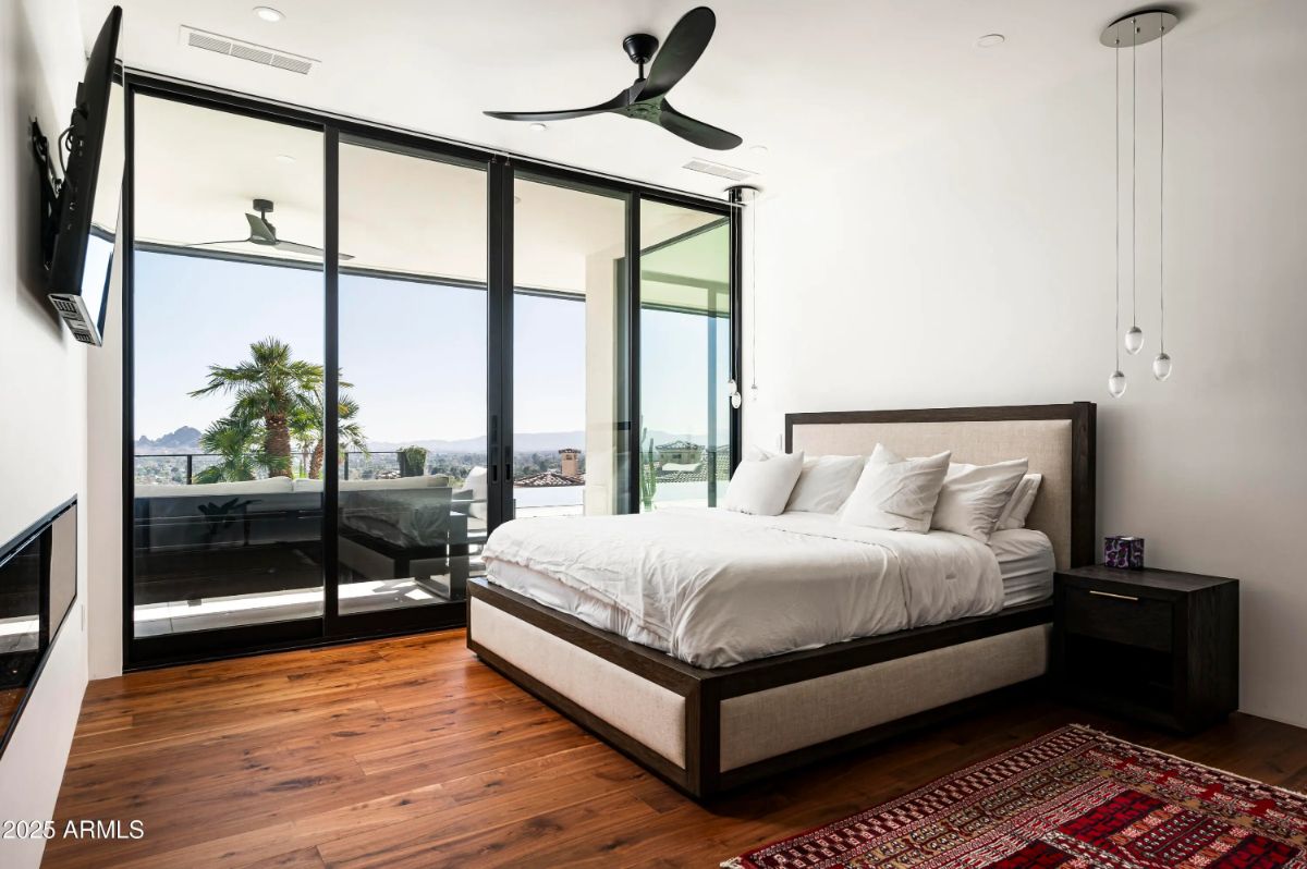 Secondary bedroom with private terrace access, ceiling fan, and glass wall showcasing distant cityscape. 