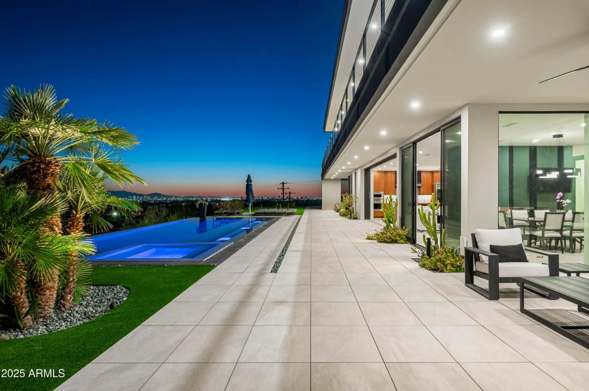 Poolside terrace with tile flooring, glass walls, and palm landscaping overlooking a city skyline at dusk. 