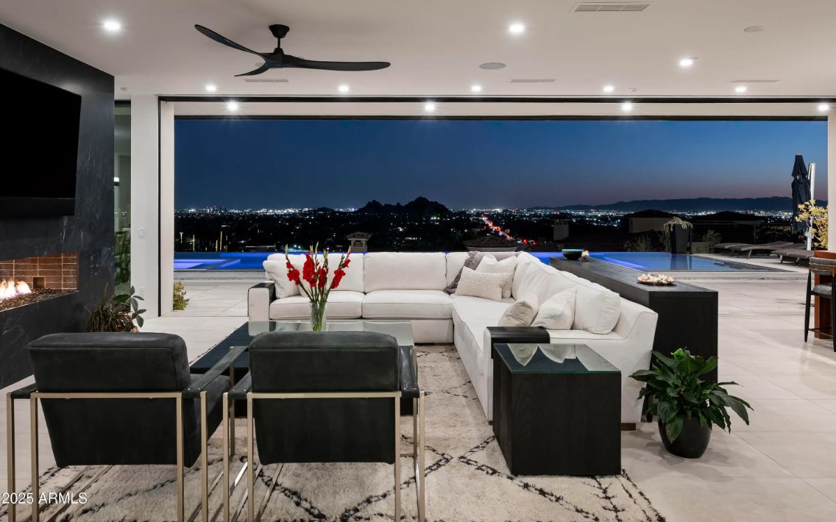 Open living area with sectional sofa, indoor-outdoor design, and panoramic nighttime city views. 