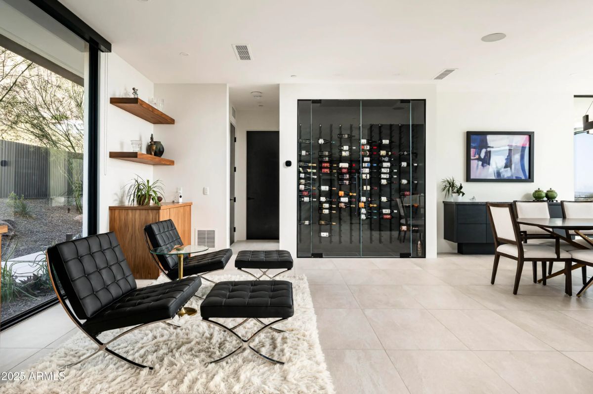 Lounge and dining space with floor-to-ceiling wine display, leather chairs, and minimalistic decor. 