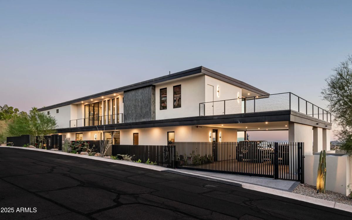 Street-facing view of contemporary home with black railing, stone accents, and gated carport entry. 