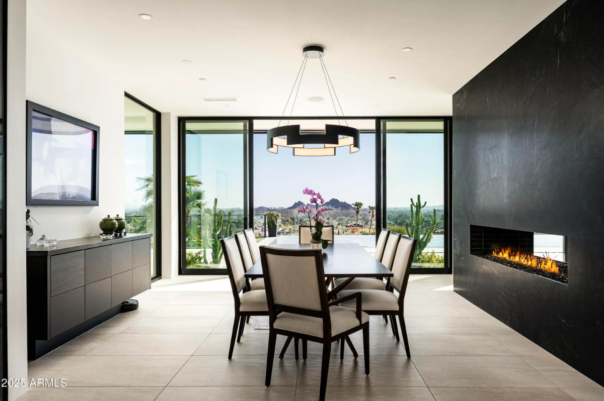 Dining room with large windows, linear chandelier, and fireplace wall facing mountain and city views. 