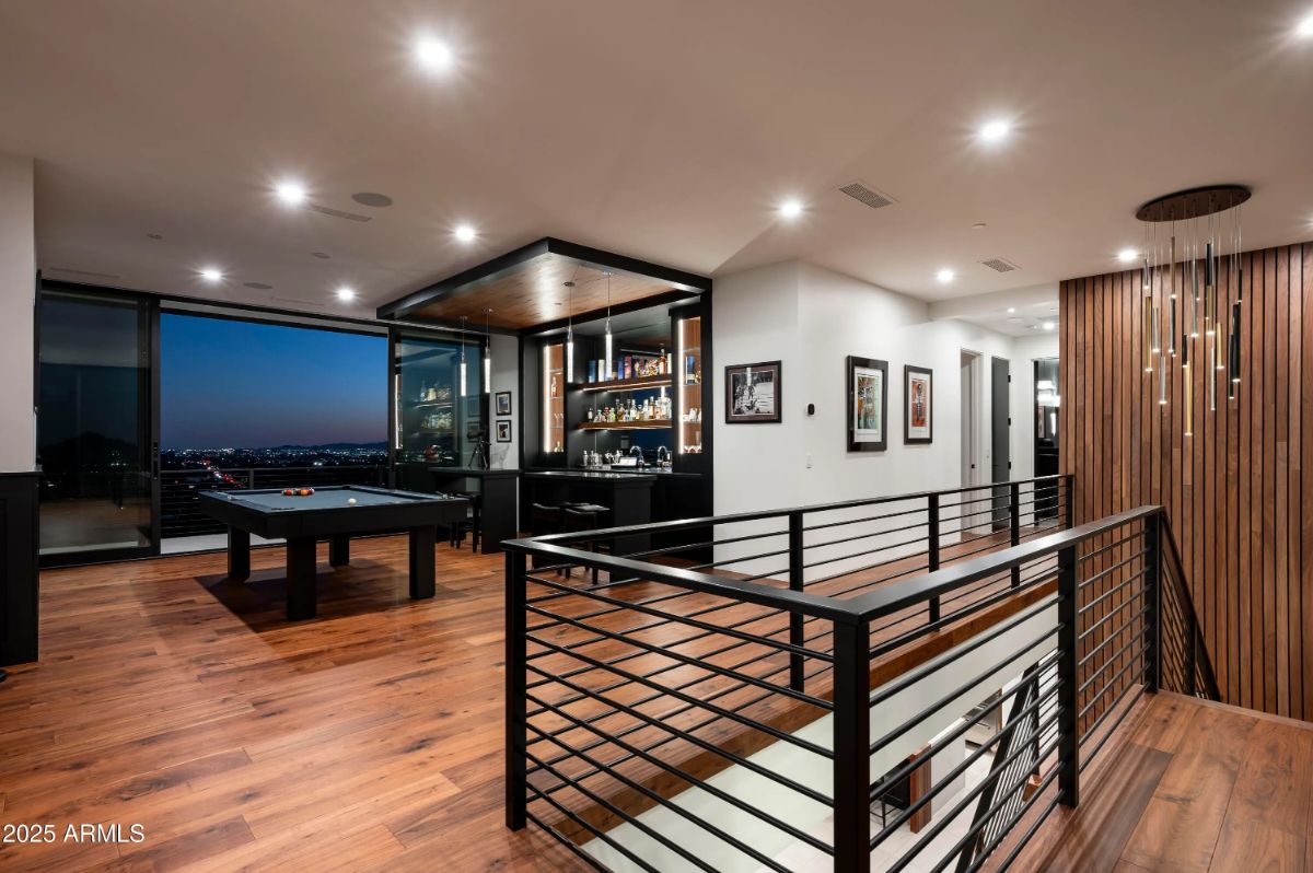 Upper-level landing with wood flooring, modern staircase, and open lounge area with a pool table and bar. 