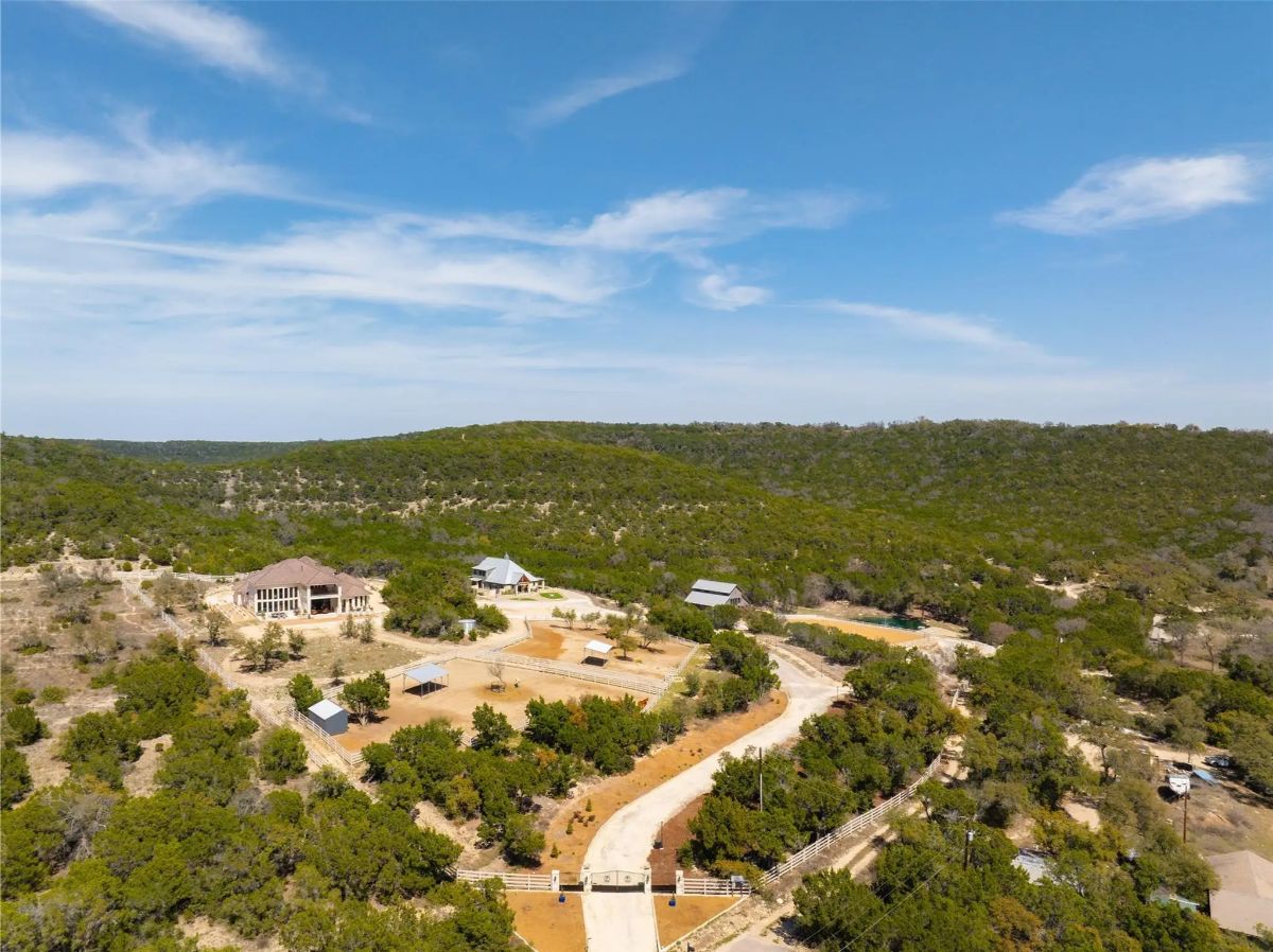 Gated entrance opens to a winding paved driveway through wooded terrain.