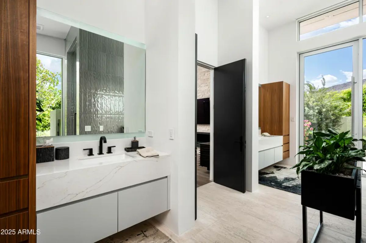 Dual-sink vanity bathroom with high ceilings, black fixtures, and outdoor garden views. 