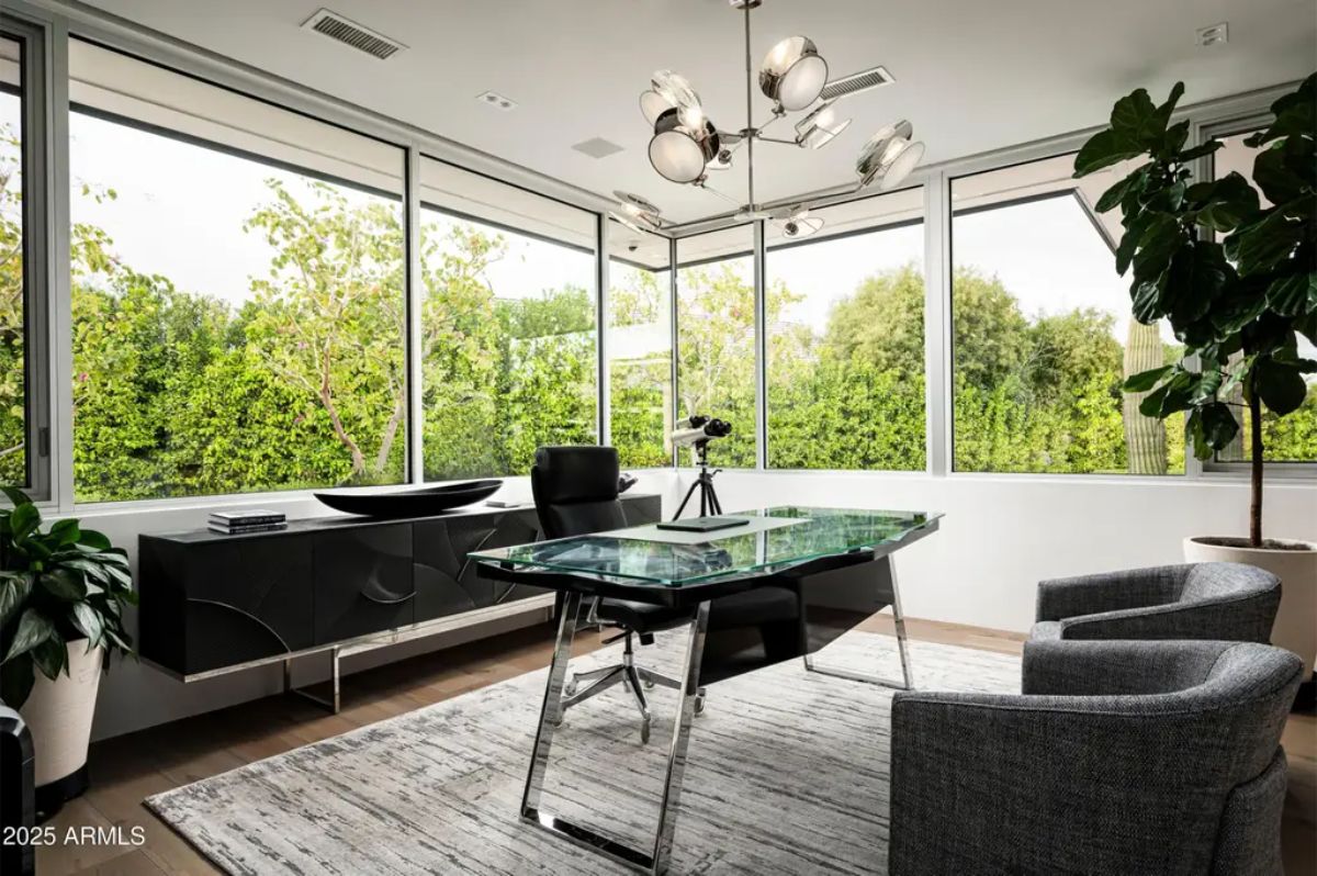 Corner office surrounded by windows offers garden views and a modern glass-top desk. 