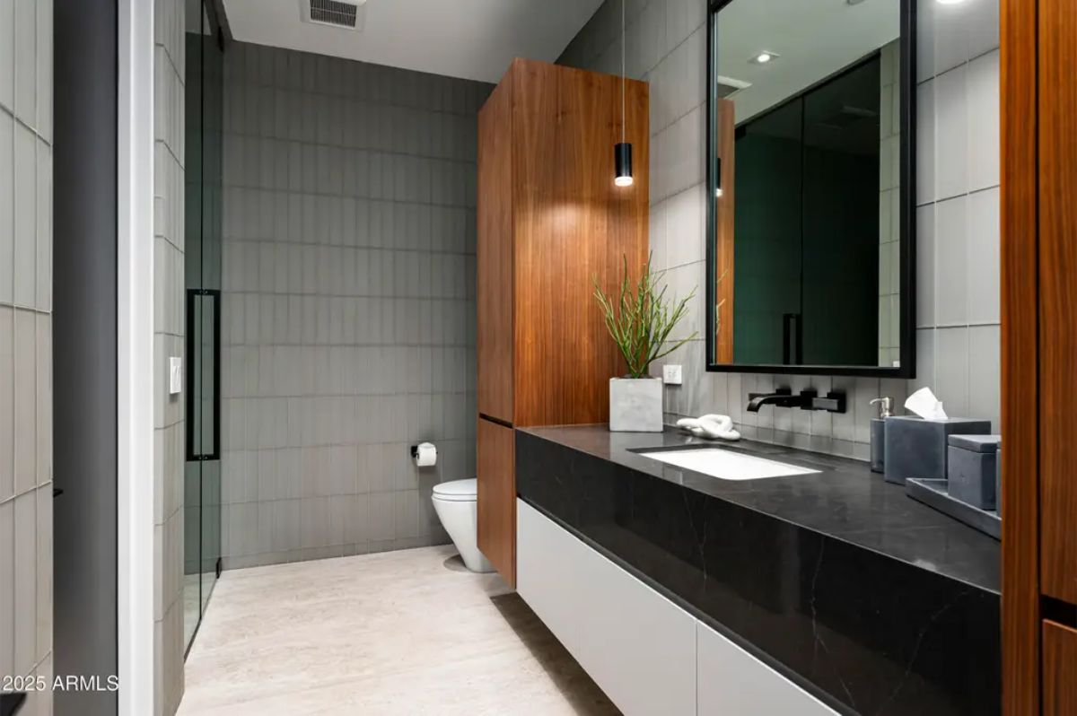Contemporary bathroom with wood cabinetry, black countertop, and a walk-in shower. 