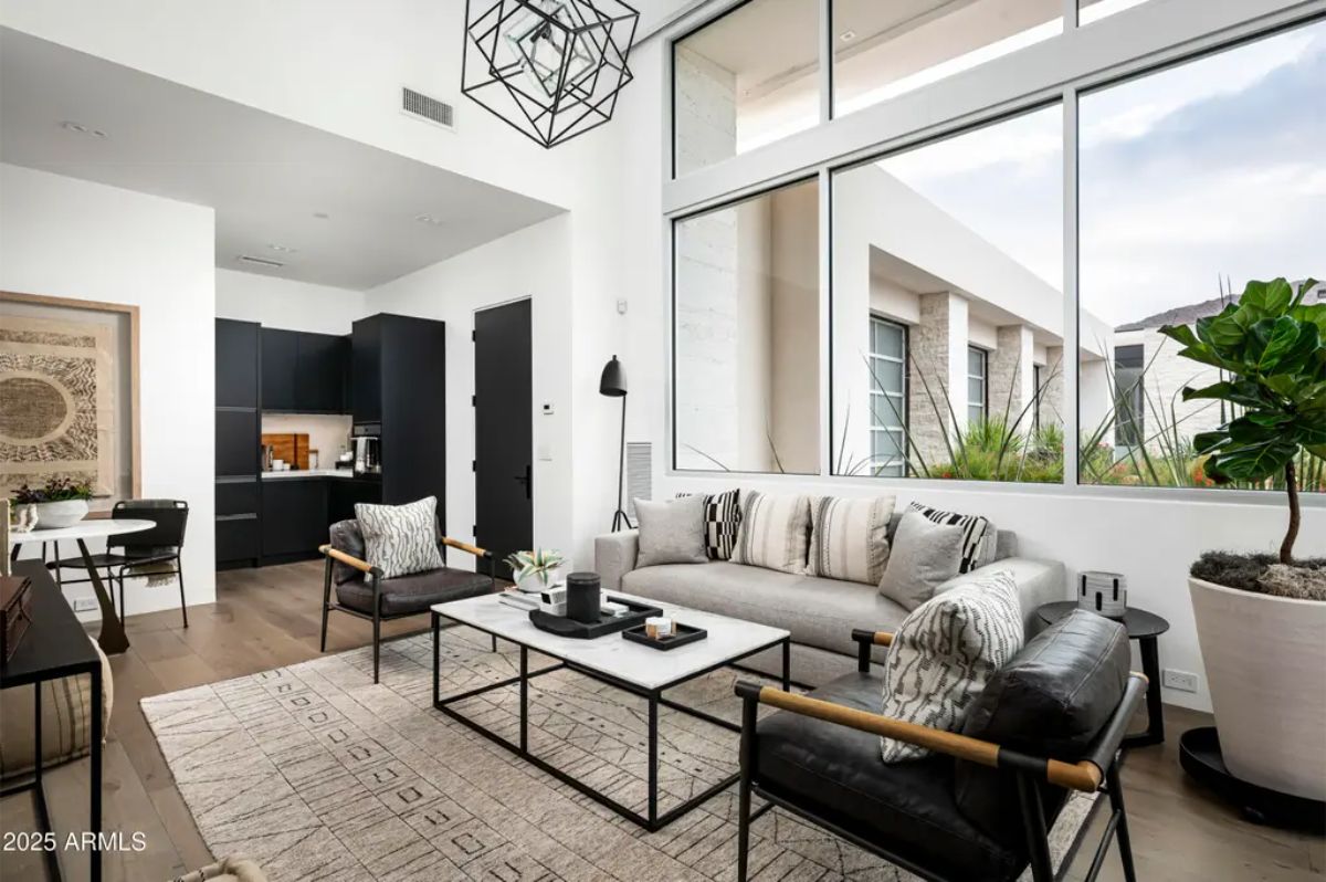Stylish sitting area with modern furniture, high windows, and adjacent kitchenette. 