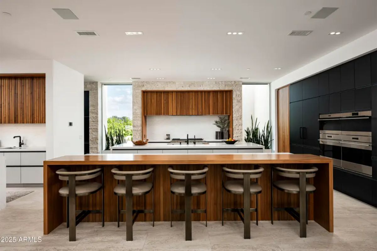 Sleek kitchen with dark accent wall, built-in appliances, and long wood island with integrated seating. 