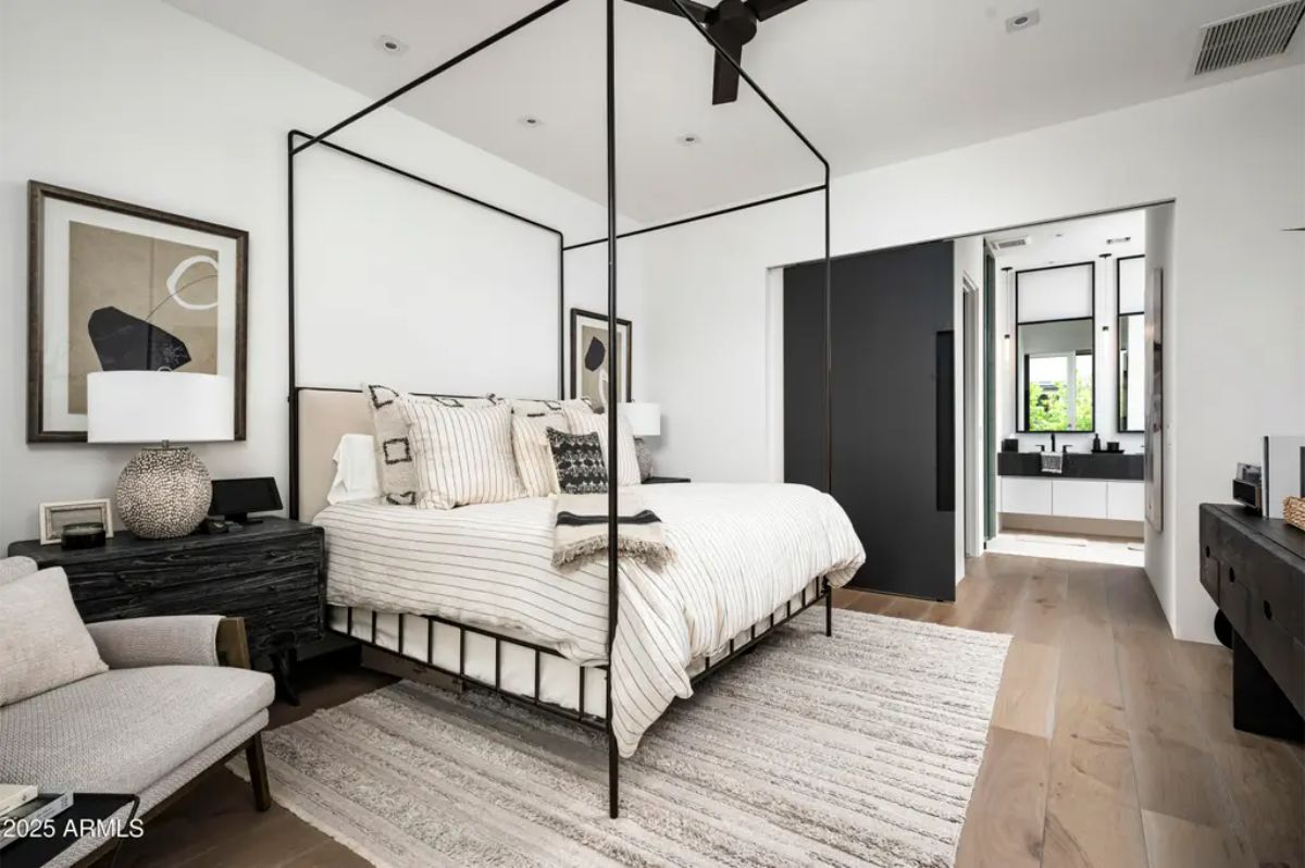 Bedroom with four-poster bed, monochrome decor, and en-suite bathroom visible through an open doorway. 