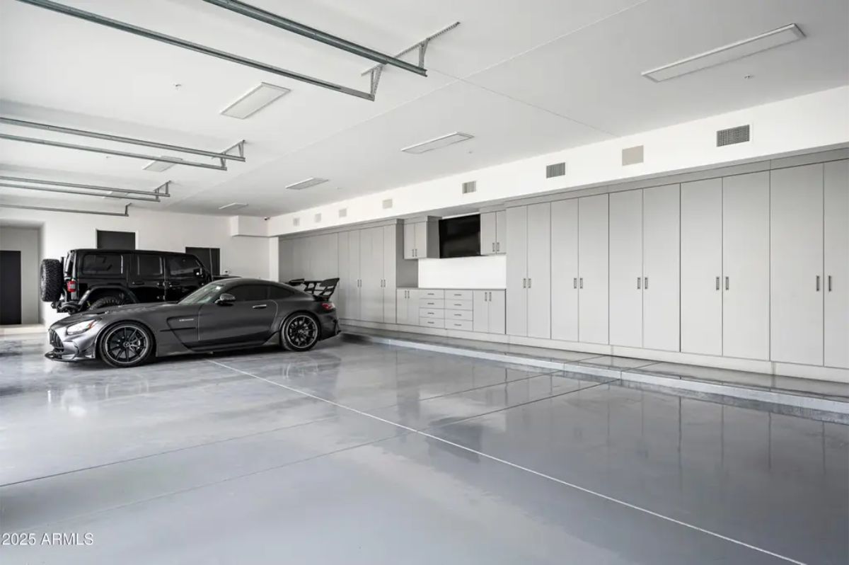 Spacious garage with glossy epoxy floors, built-in cabinetry, and luxury vehicles parked along the back wall. 