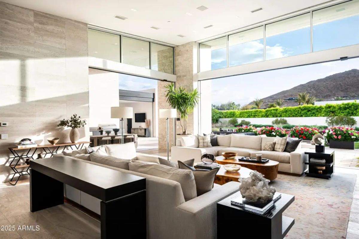 Living room features tall ceilings, large sectional, and full-height sliding glass doors opening to a mountain view. 