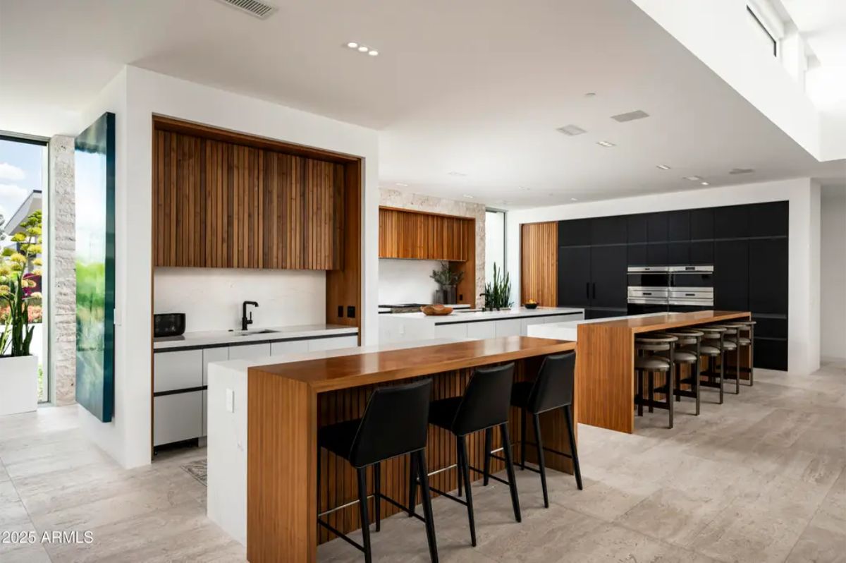Streamlined kitchen includes two-tone wood cabinetry, dual islands, and integrated appliances. 