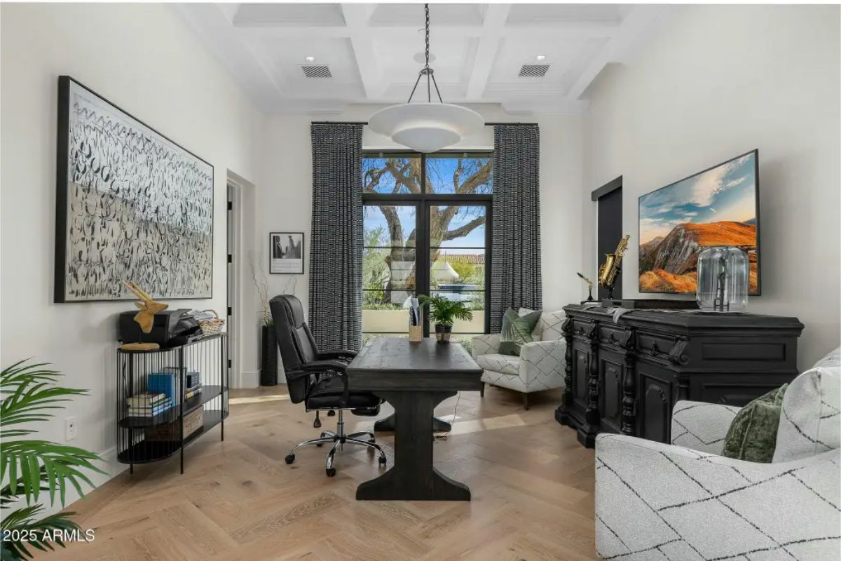 Office with coffered ceiling, dark furniture, seating area, and window view of front garden. 