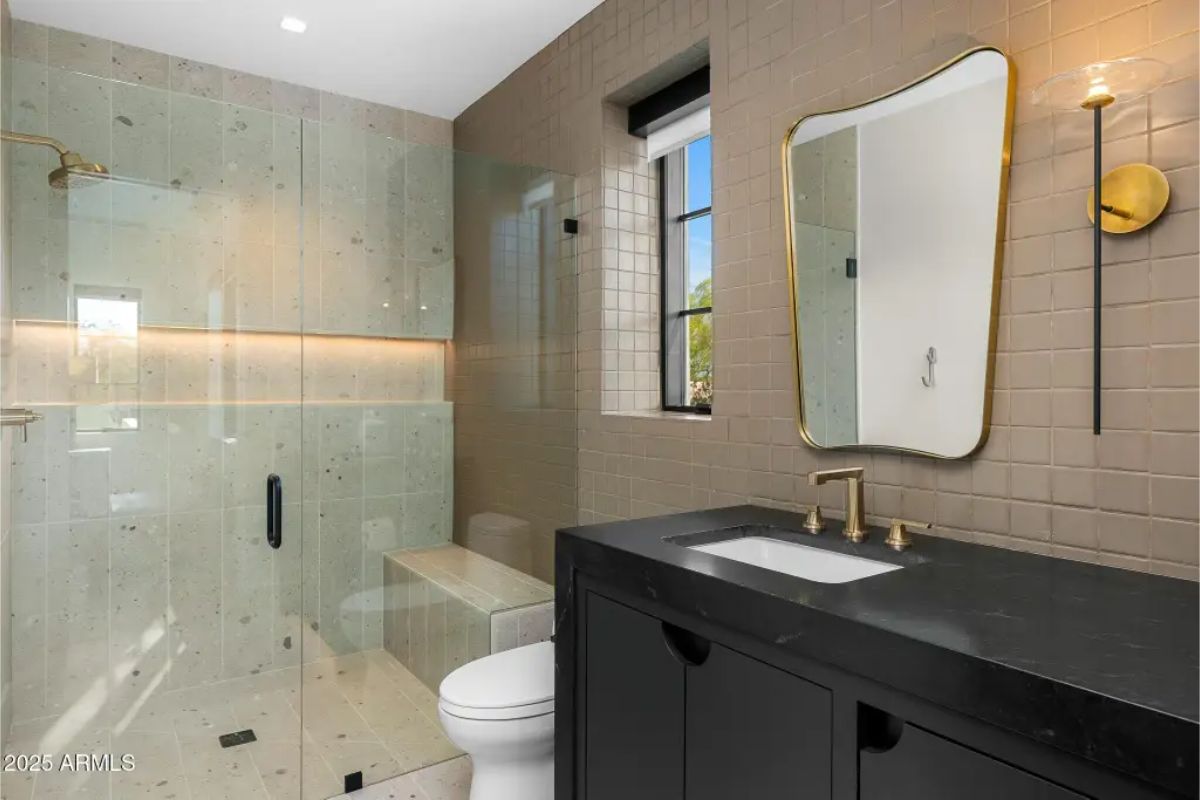 Compact bathroom with walk-in shower, dark vanity, brass fixtures, and textured wall tile. 