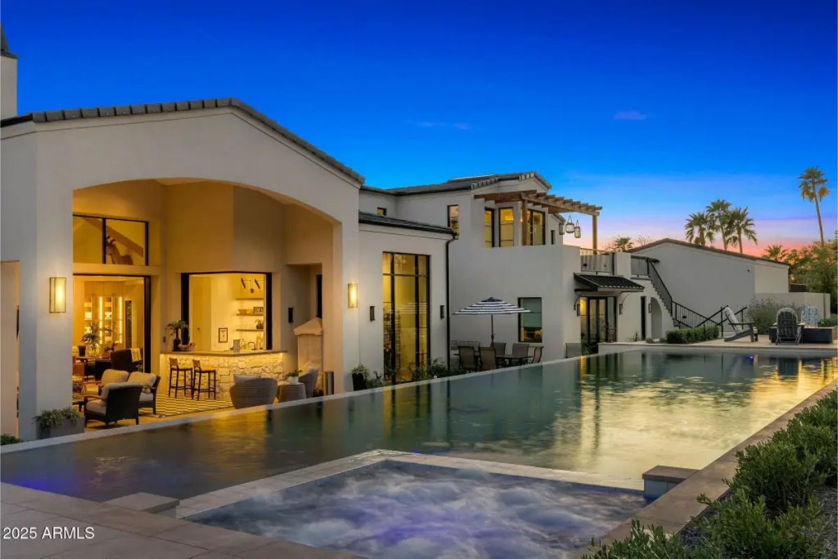 Twilight view of luxury home with covered patio, infinity-edge pool, and elevated spa. 