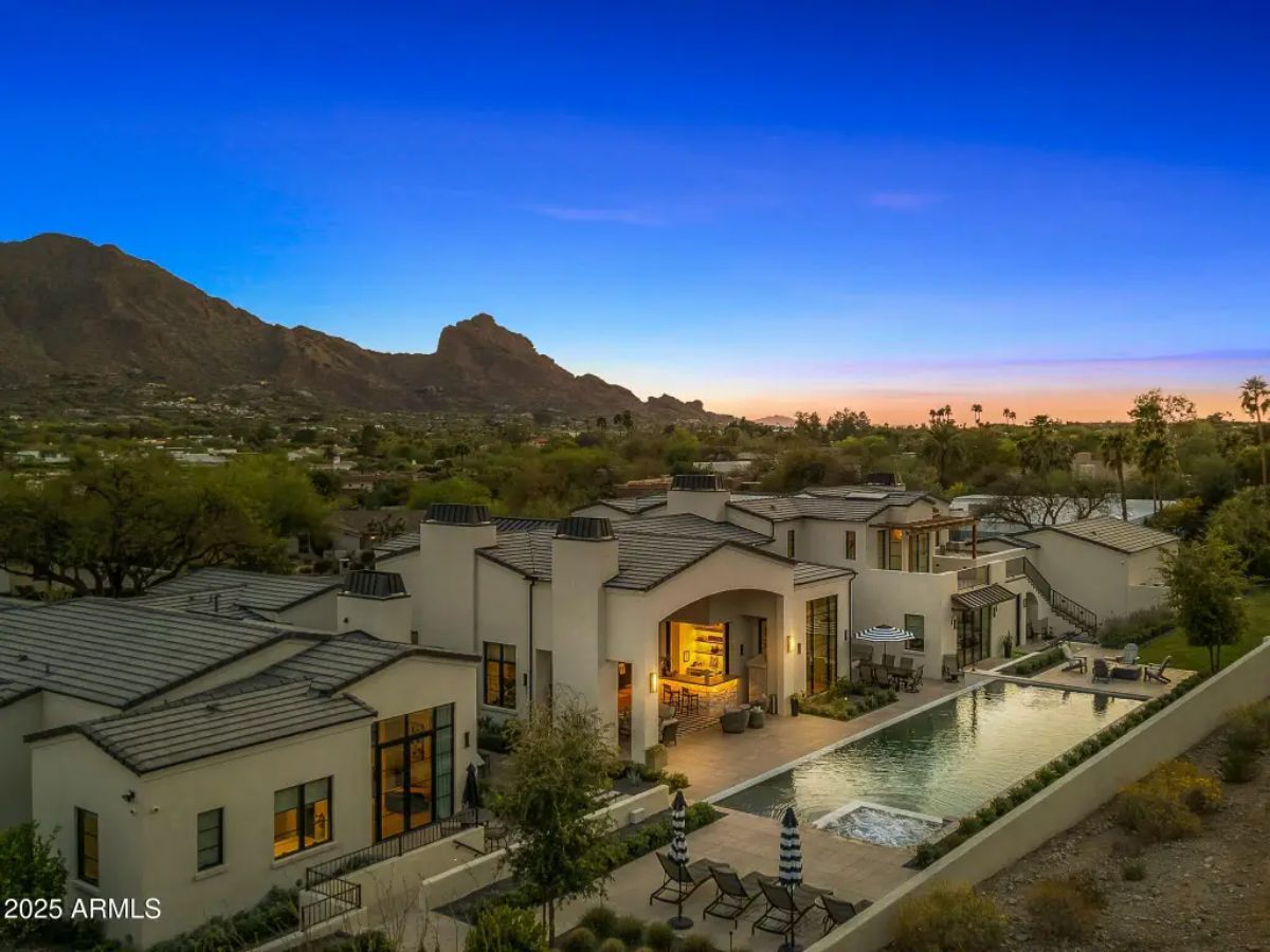Aerial dusk shot of expansive residence with long lap pool, mountain backdrop, and multi-level layout. 
