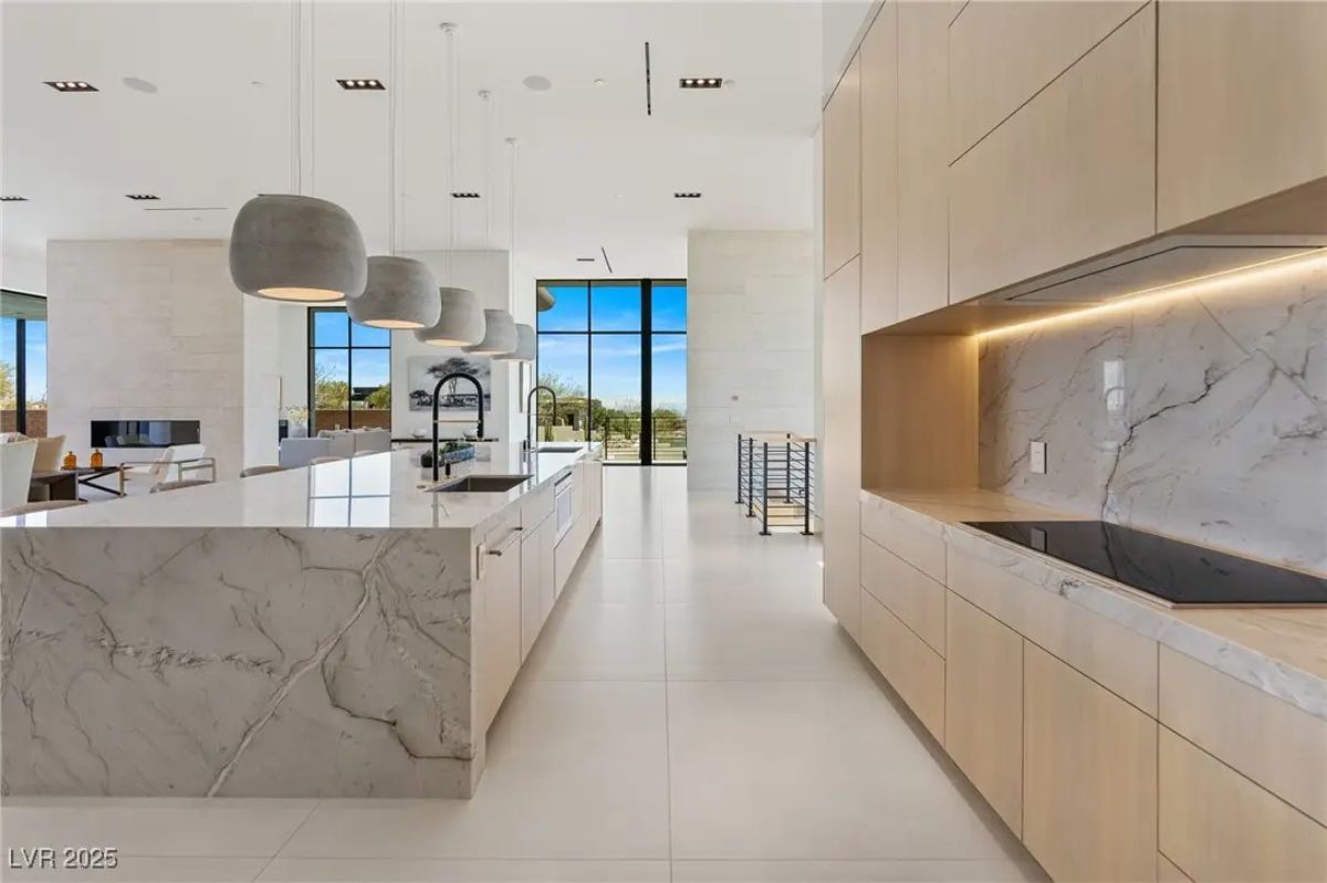 Alternate kitchen view with integrated appliances, light wood cabinetry, and large windows. 