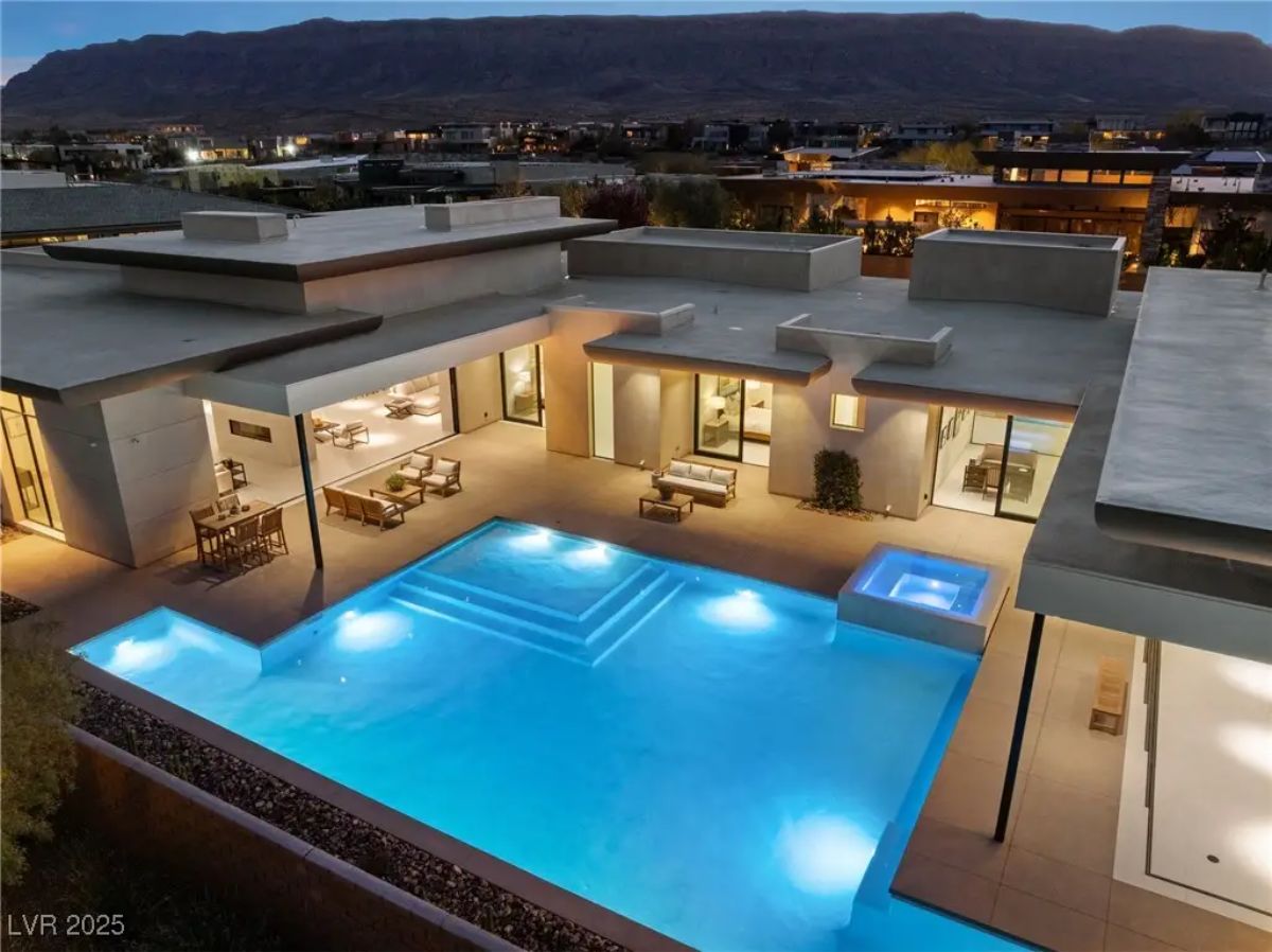 Elevated nighttime view of contemporary home with illuminated pool, spa, and patio areas. 