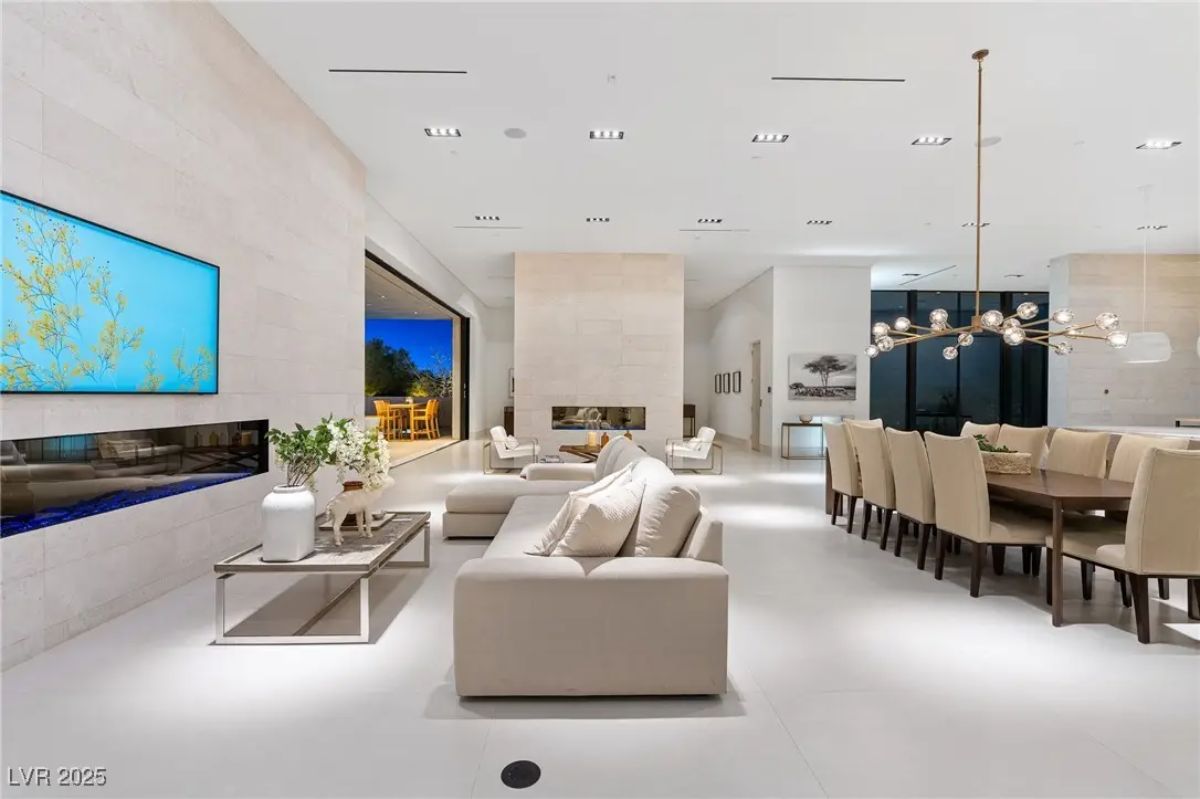 Open-concept living and dining area with neutral furnishings, double-sided fireplace, and high ceilings. 