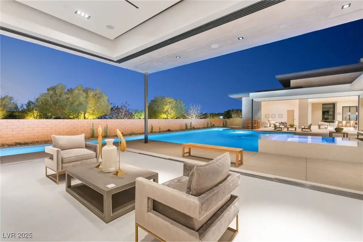 Covered outdoor lounge with modern furniture and view of pool and landscaped yard. 