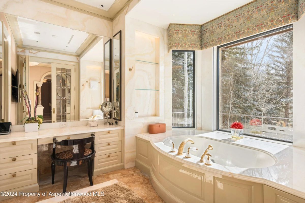 Bright bathroom with soaking tub, makeup vanity, and large window with forest views. 