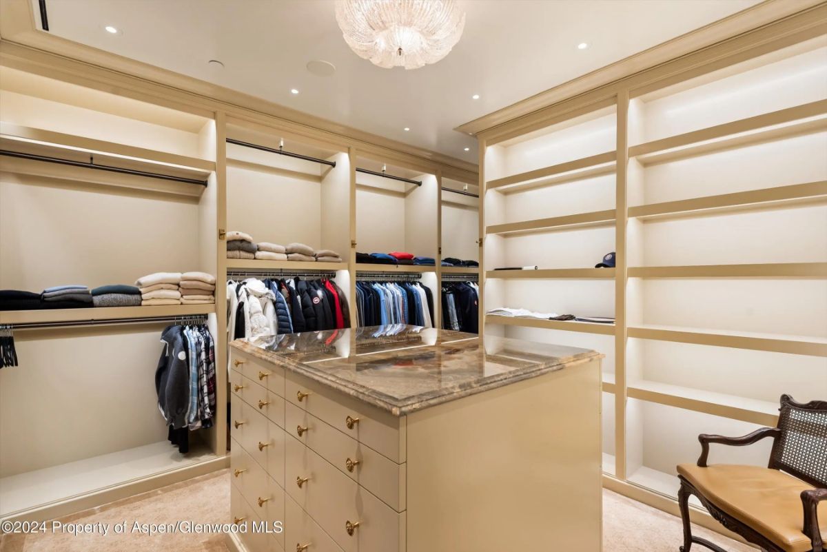 Walk-in closet with built-in shelving, display island, and overhead chandelier. 