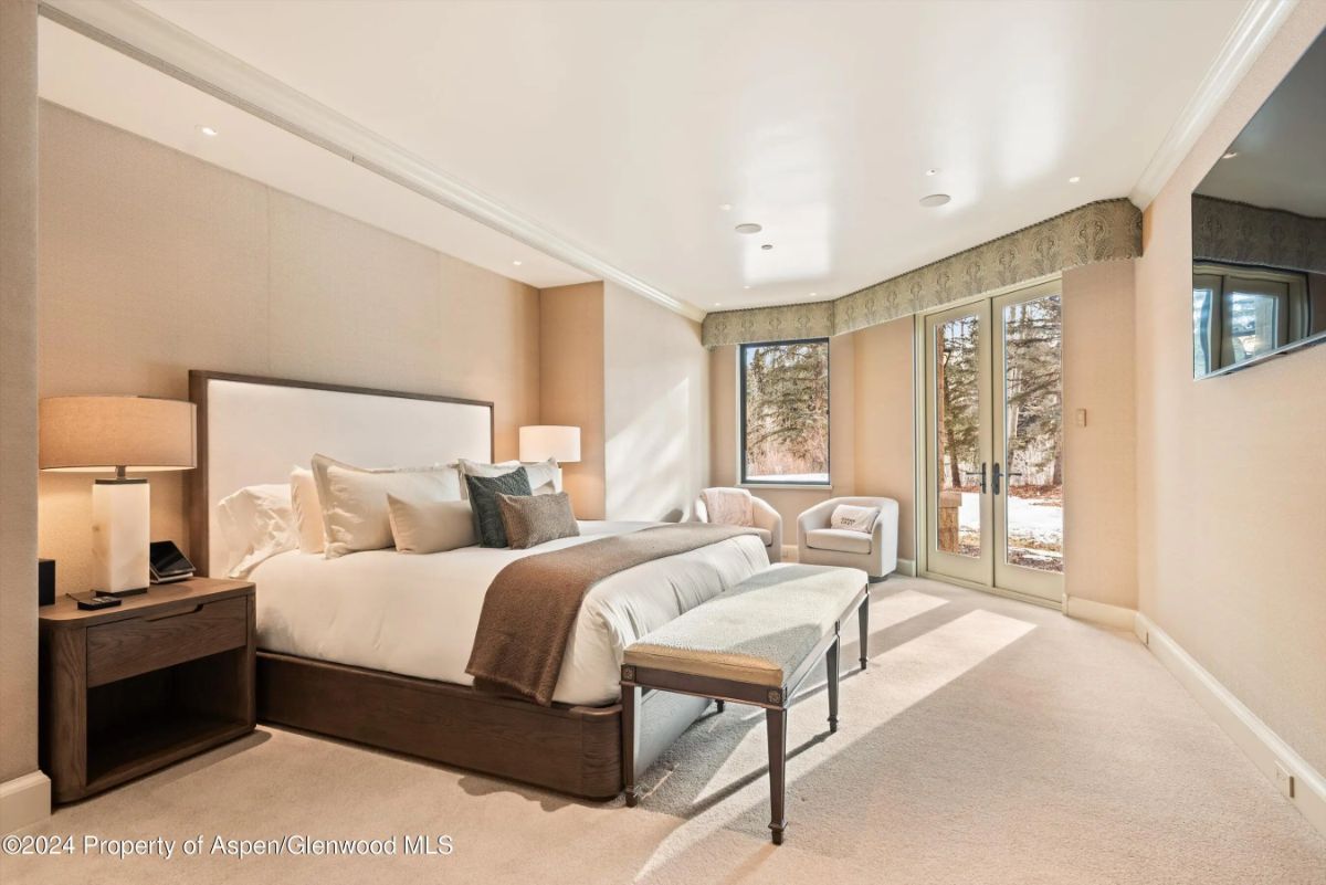 Bedroom with neutral tones, upholstered bed, and glass door opening to snowy outdoor scenery. 