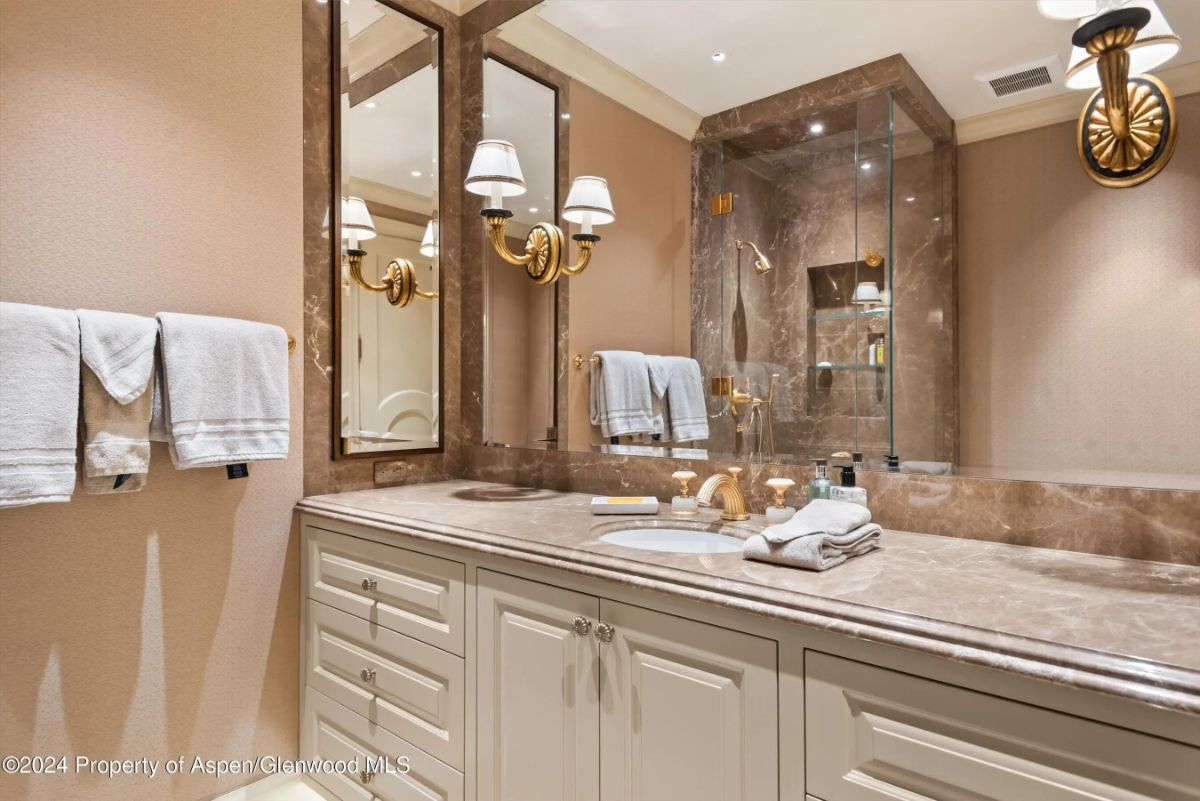 Double vanity bathroom with marble countertops and glass-enclosed shower. 