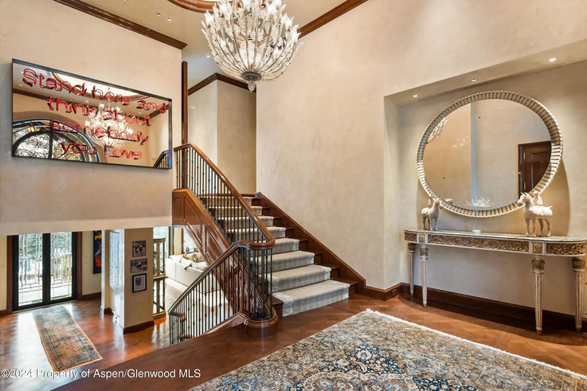 Entry hall with wood floors, a circular mirror console, and decorative chandelier over rug. 