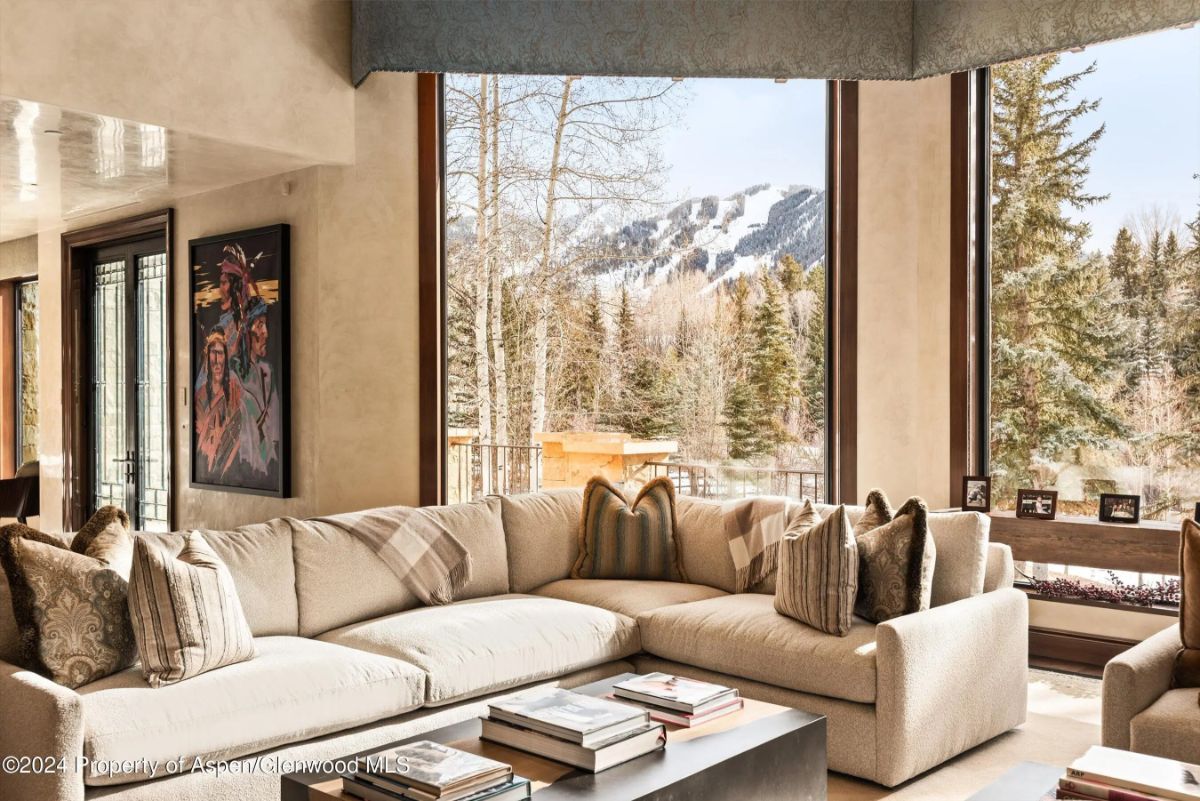 Cozy seating area with L-shaped sofa and mountain views framed by tall corner windows. 