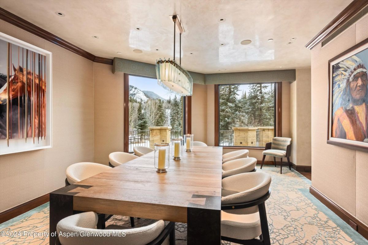 Dining room with wood table, upholstered chairs, and full-height windows overlooking the forest. 