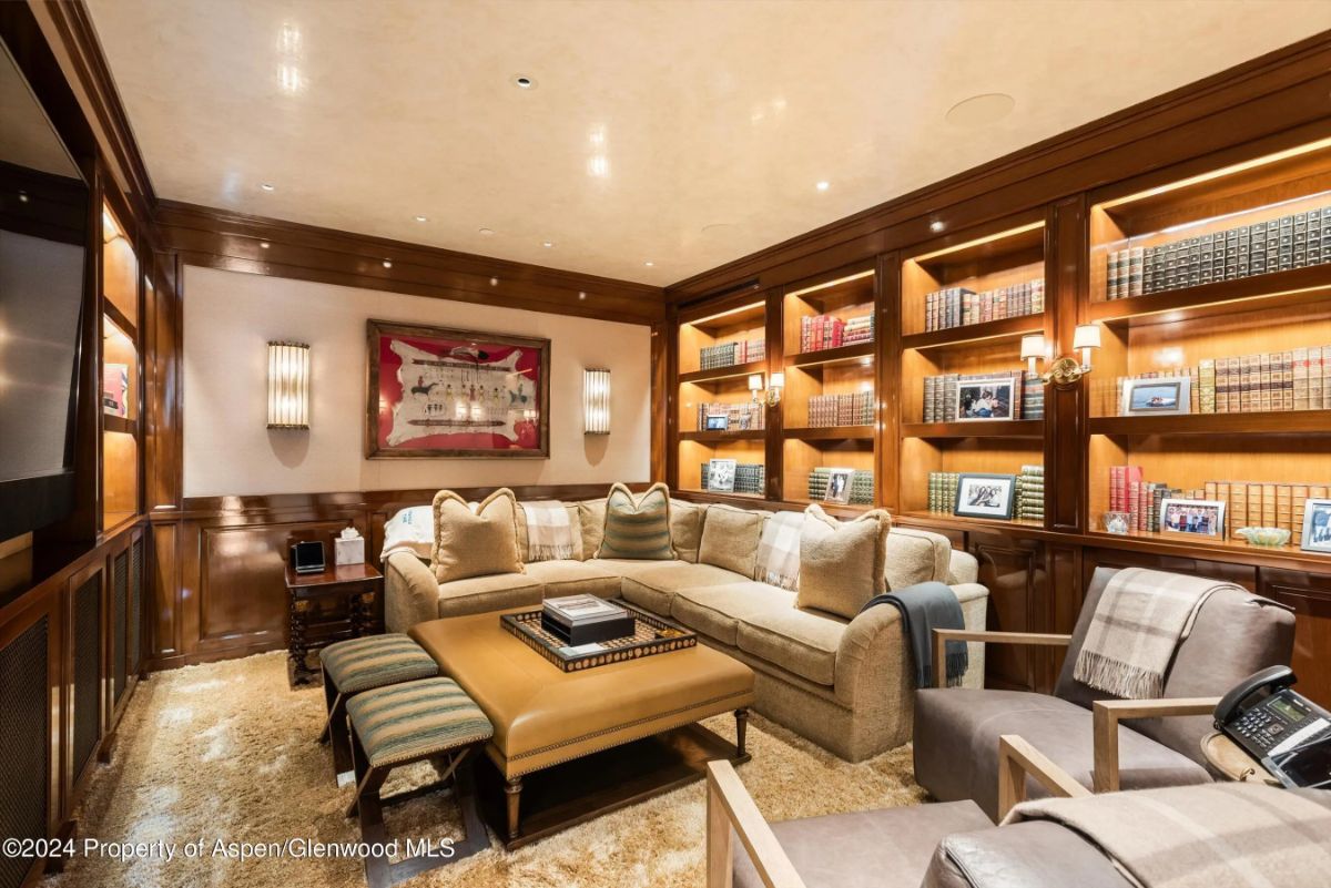 Cozy library lounge with wraparound sofa, illuminated bookshelves, and wall art. 