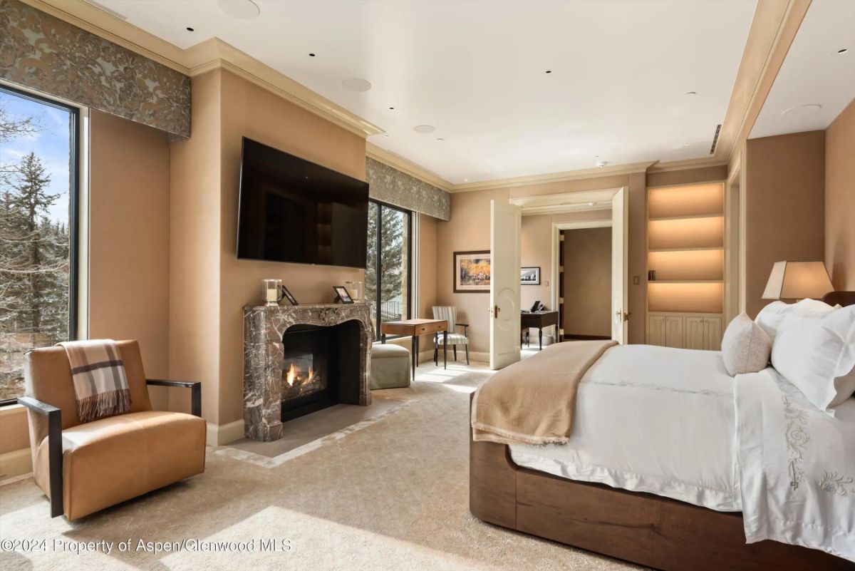 Fireplace bedroom suite with built-in shelving, large windows, and soft beige walls and carpet. 