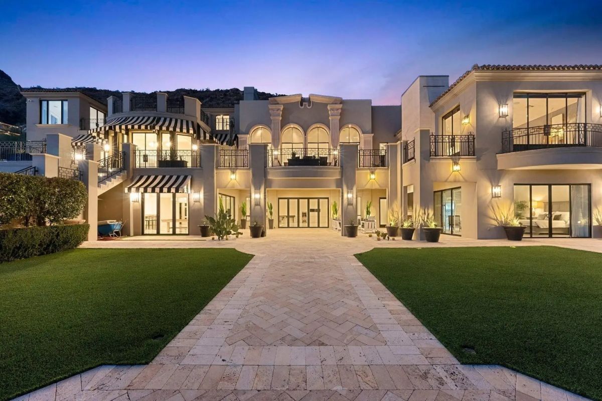Symmetrical rear façade with tall arched windows, manicured lawn, and marble-tiled pathway. 