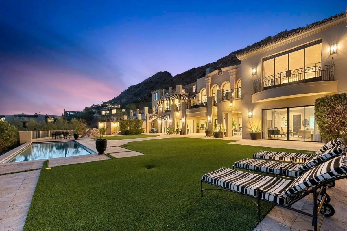 Evening view of the estate with striped loungers, manicured lawn, and glowing facade set against the hillside. 