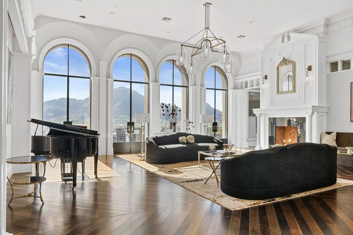 Living room with arched windows, black velvet sofas, fireplace, and dramatic mountain views. 